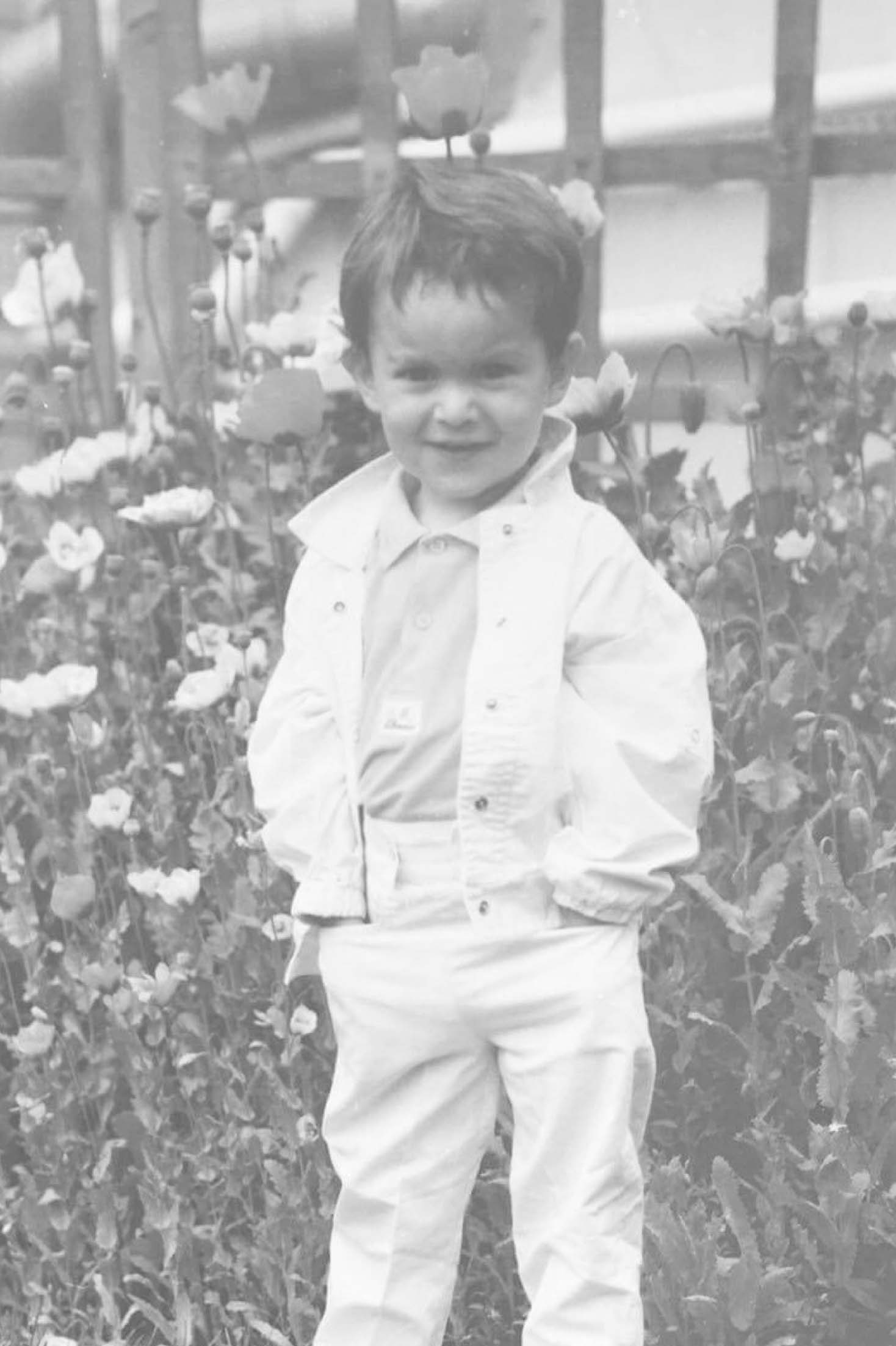 A photo of myself as a young boy, hands in pockets in front of some flowers looking cheeky.